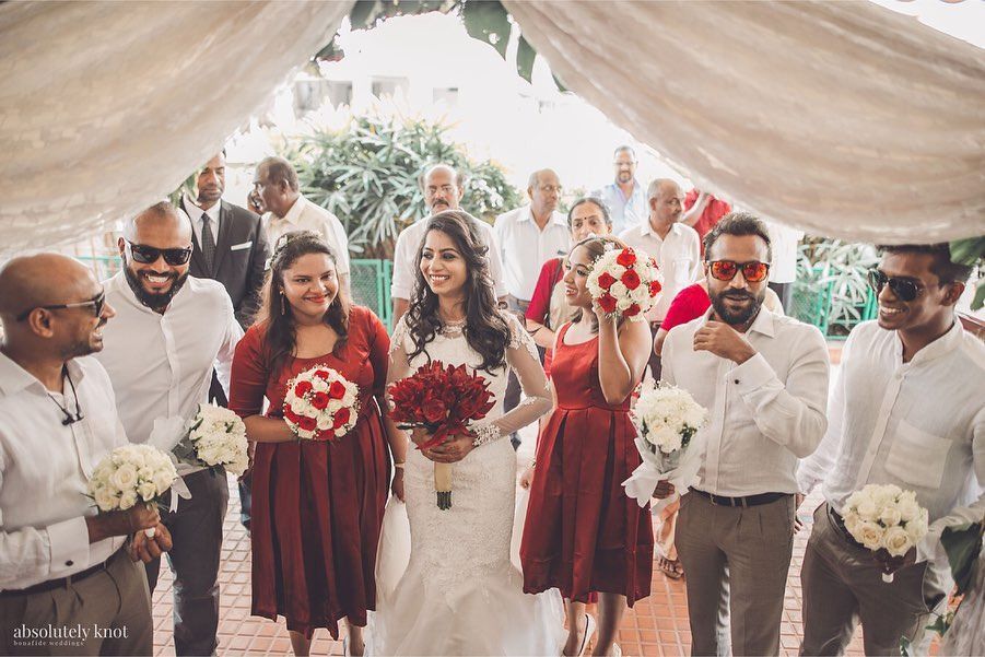 Bridesmaids and family walking out under a draped canopy, holding bouquets