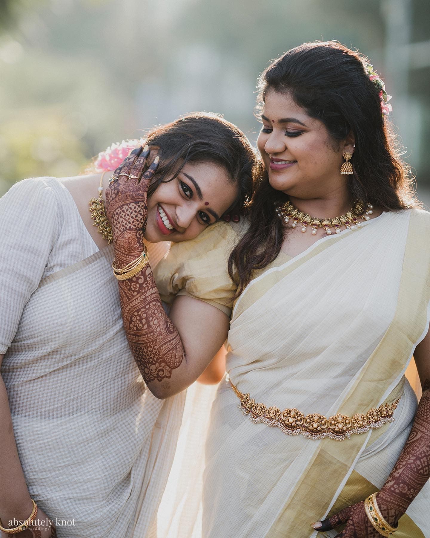 Two women in kasavu sarees laughing, cheek to cheek