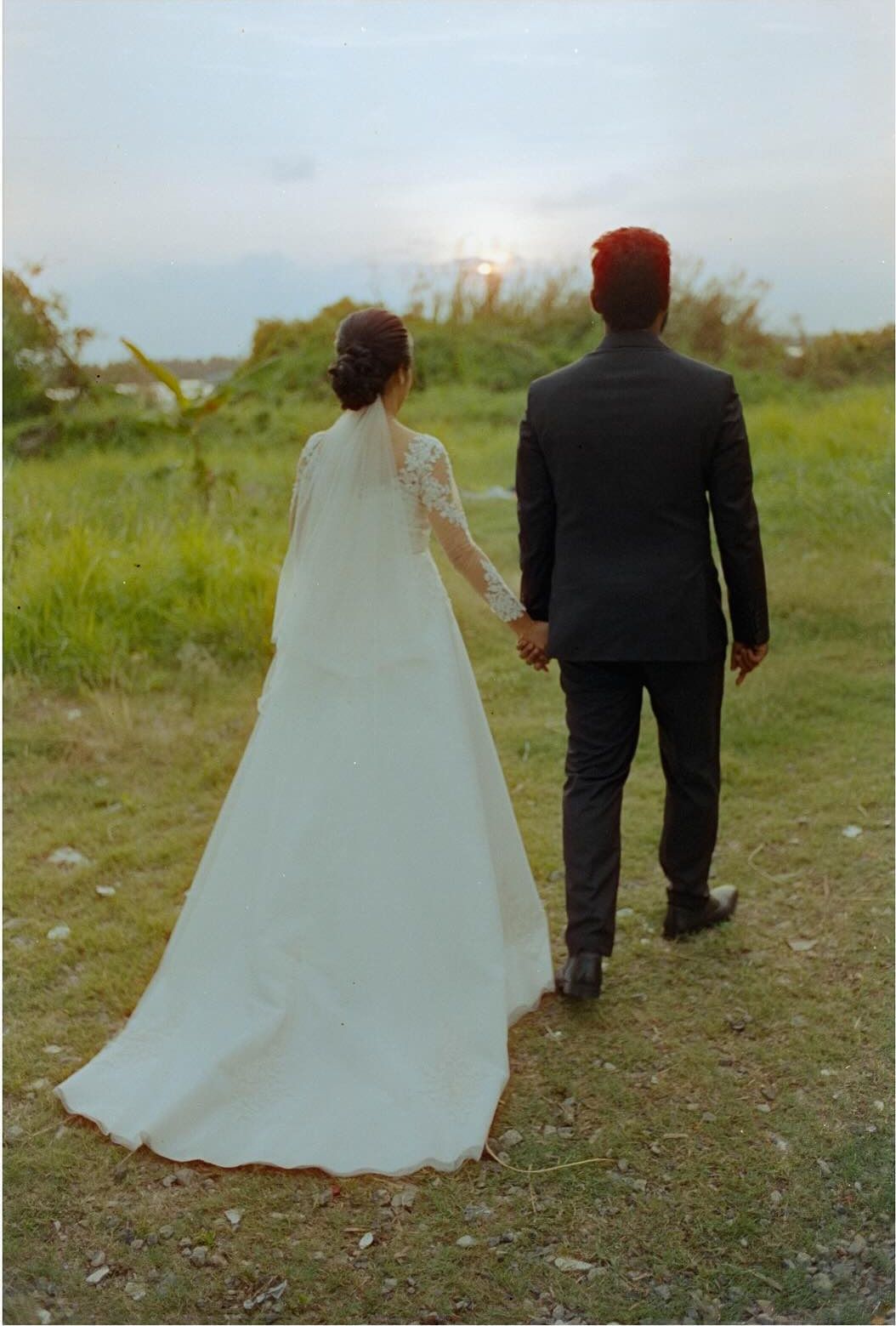 A bride and groom walking away across a field at dusk, shot on CineStill 800T