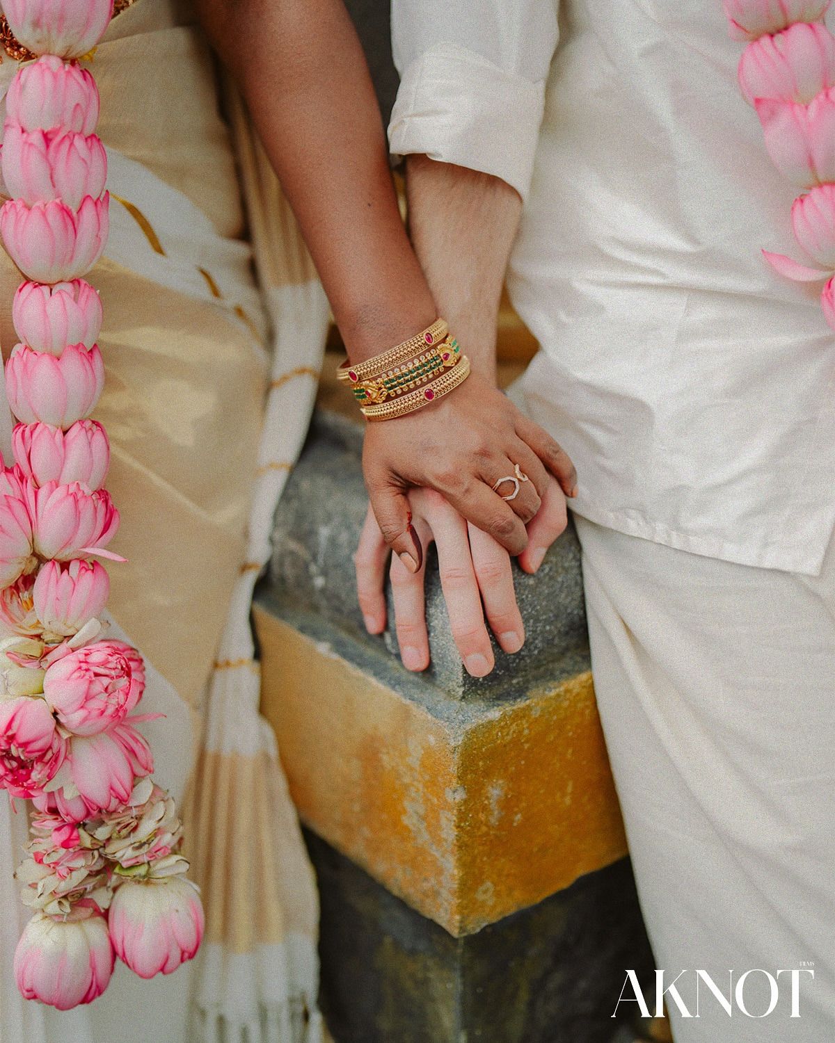 The couple’s hands resting together beside jasmine and rose garlands