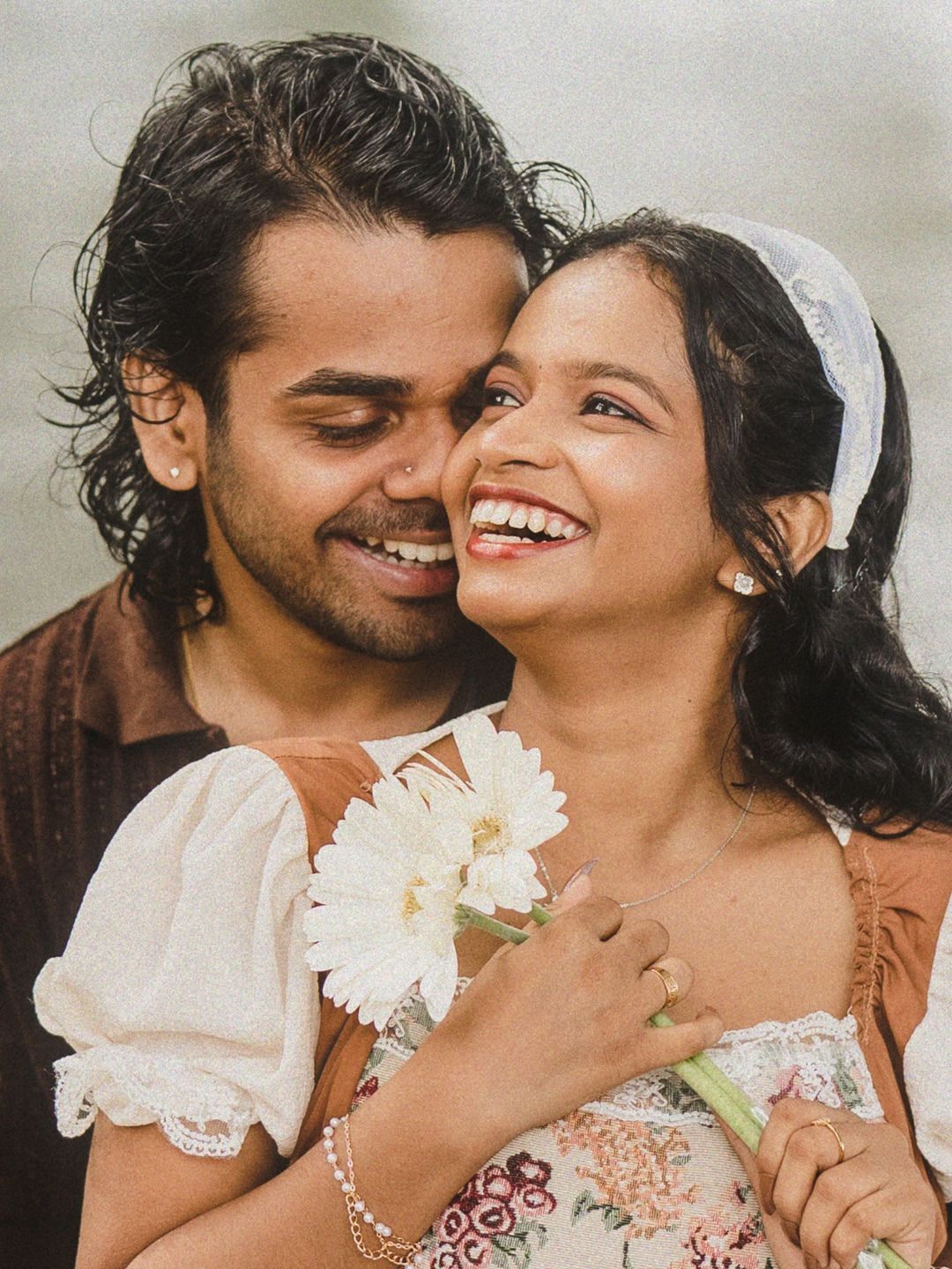 A couple laughing, the bride holding white daisies