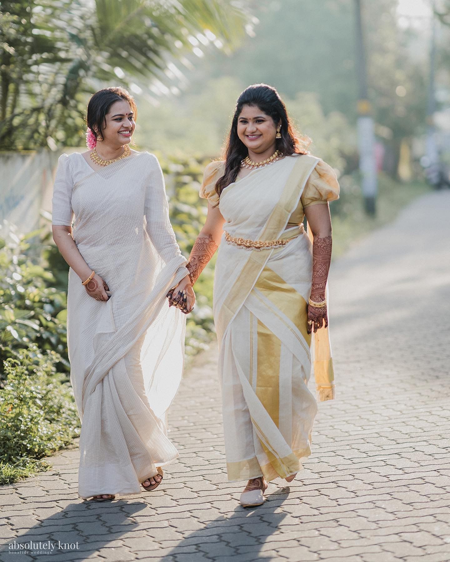 Two women in sarees walking together down a paved lane