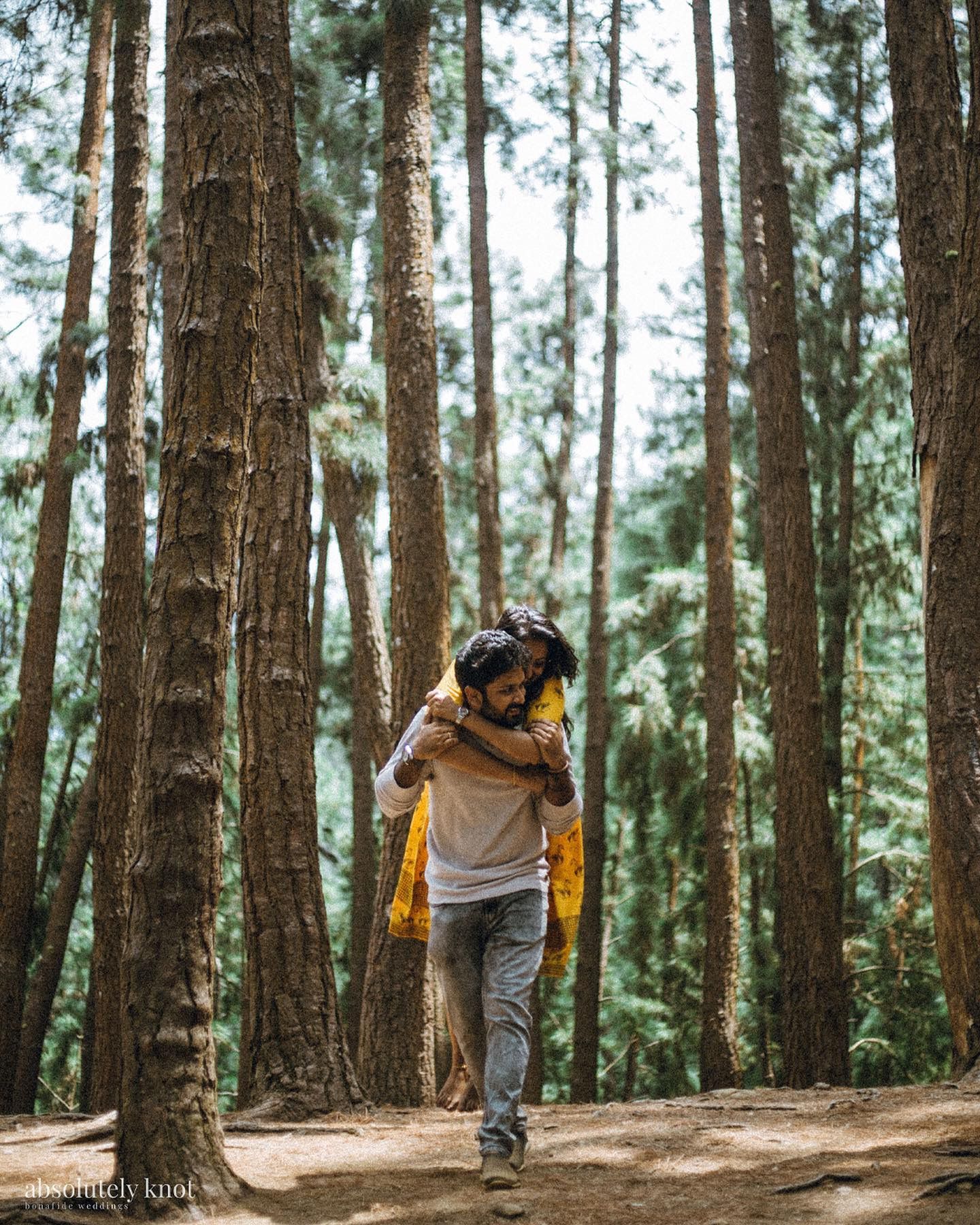 A man carrying his partner on his back through a pine forest