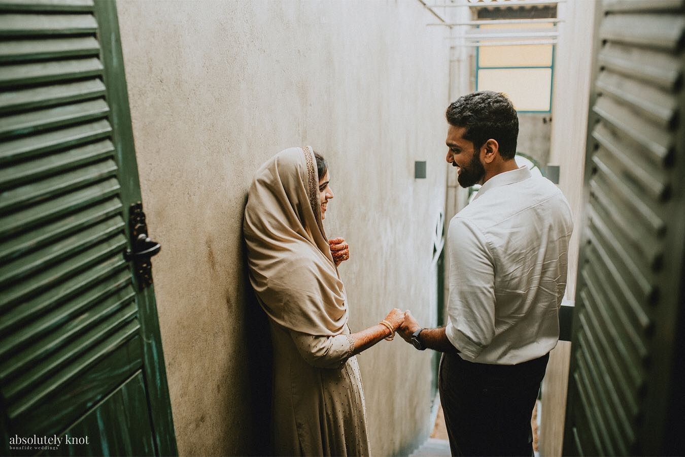A couple meeting in a narrow passage between green shutters